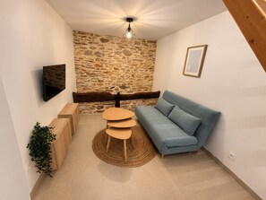Un salon moderne avec un mur en pierre, un canapé bleu, une table basse en bois et un téléviseur fixé au mur.