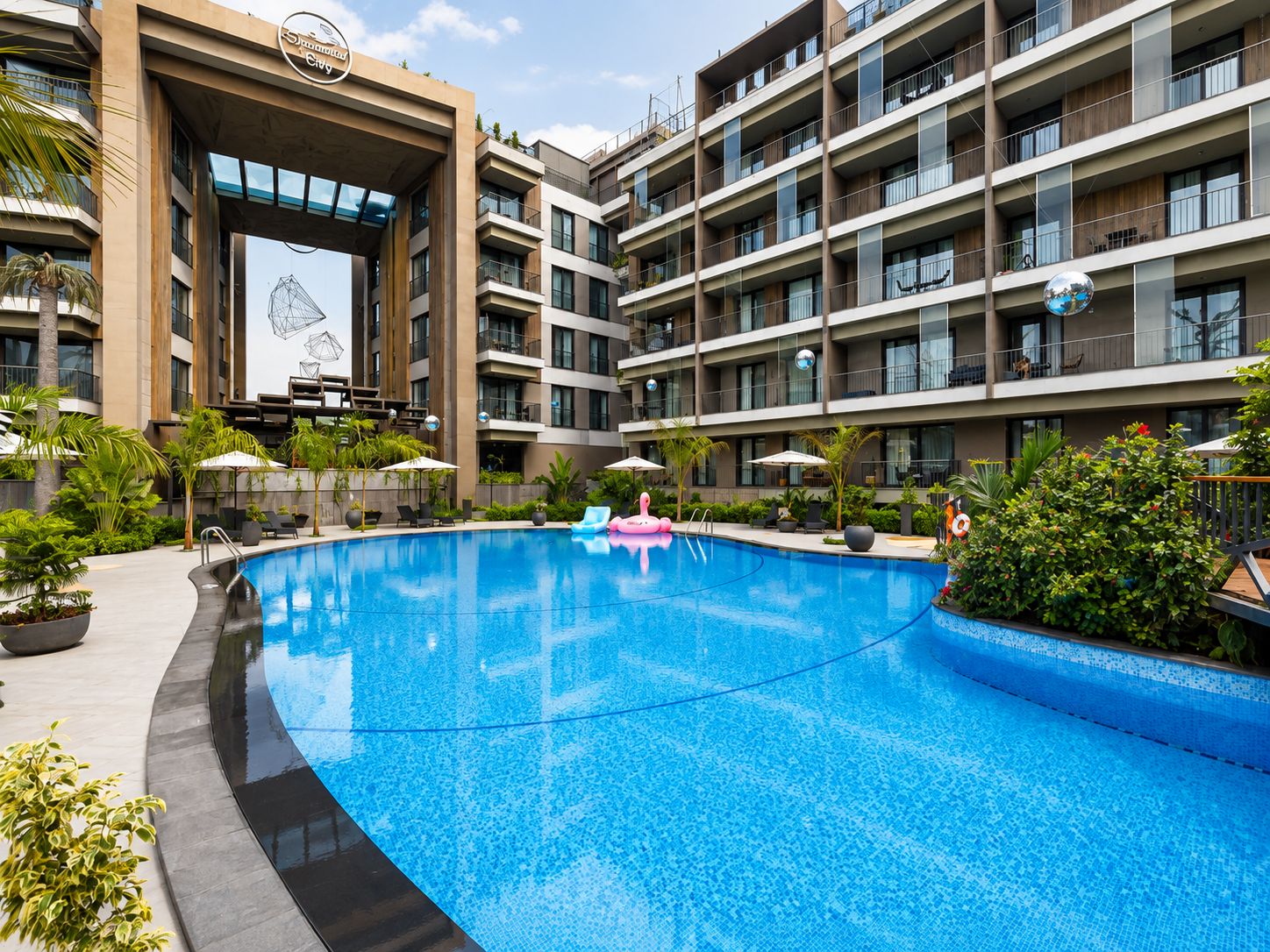 A modern hotel with a swimming pool, multiple balconies, and outdoor seating areas.
