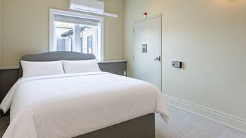 Ein Hotelzimmer mit Bett, Fenster, Klimaanlage, einer Tür mit einem Schild und einem Lichtschalter.