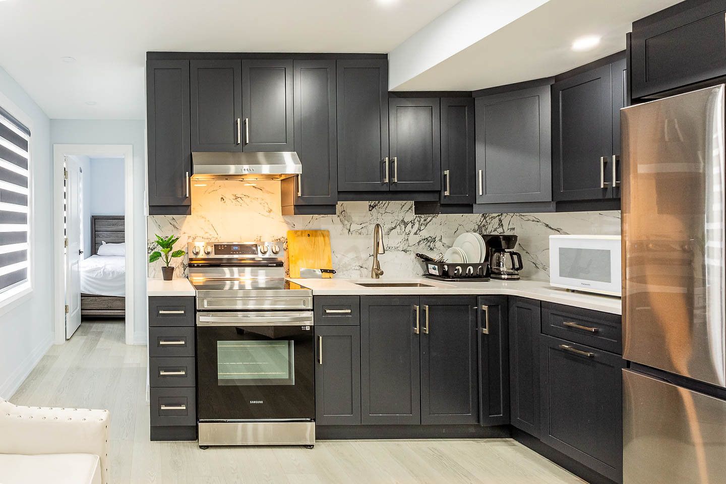A modern kitchen with dark cabinetry, stainless steel appliances, and a marble backsplash.