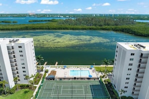 A high-rise building with a rooftop pool and tennis courts, overlooking a body of water with greenery and distant buildings. - 7th-Floor Bay & Gulf Views - Near Turtle Beach (Siesta Key)