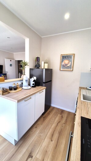 A modern kitchen with white cabinetry, a black refrigerator, a coffee machine, and a framed coffee advertisement on the wall. - HappyHaven – Stylish Apartment Just a Few Steps from the Ocean (Blankenberge)