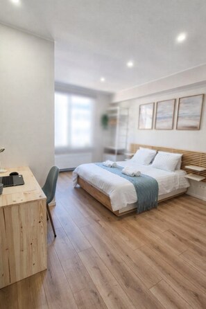 A modern bedroom with a wooden desk, a bed with white bedding, and a view of the outdoors through a window. - HappyHaven – Stylish Apartment Just a Few Steps from the Ocean (Blankenberge)