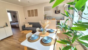 A modern living space with a dining area, a grey sofa, and a kitchen in the background. - HappyHaven – Stylish Apartment Just a Few Steps from the Ocean (Blankenberge)