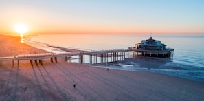 A pier extending into calm waters with a building at the end, overlooking a beach. - HappyHaven – Stylish Apartment Just a Few Steps from the Ocean (Blankenberge)