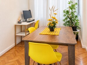 Ein Essbereich mit einem Holztisch, gelben Stühlen, einem Computer auf einem Schreibtisch und einer Topfpflanze.