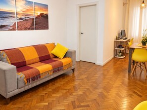 Ein Wohnzimmer mit einer Couch, einem Esstisch mit Stühlen, einer Tür und einer Wand mit drei gerahmten Bildern.