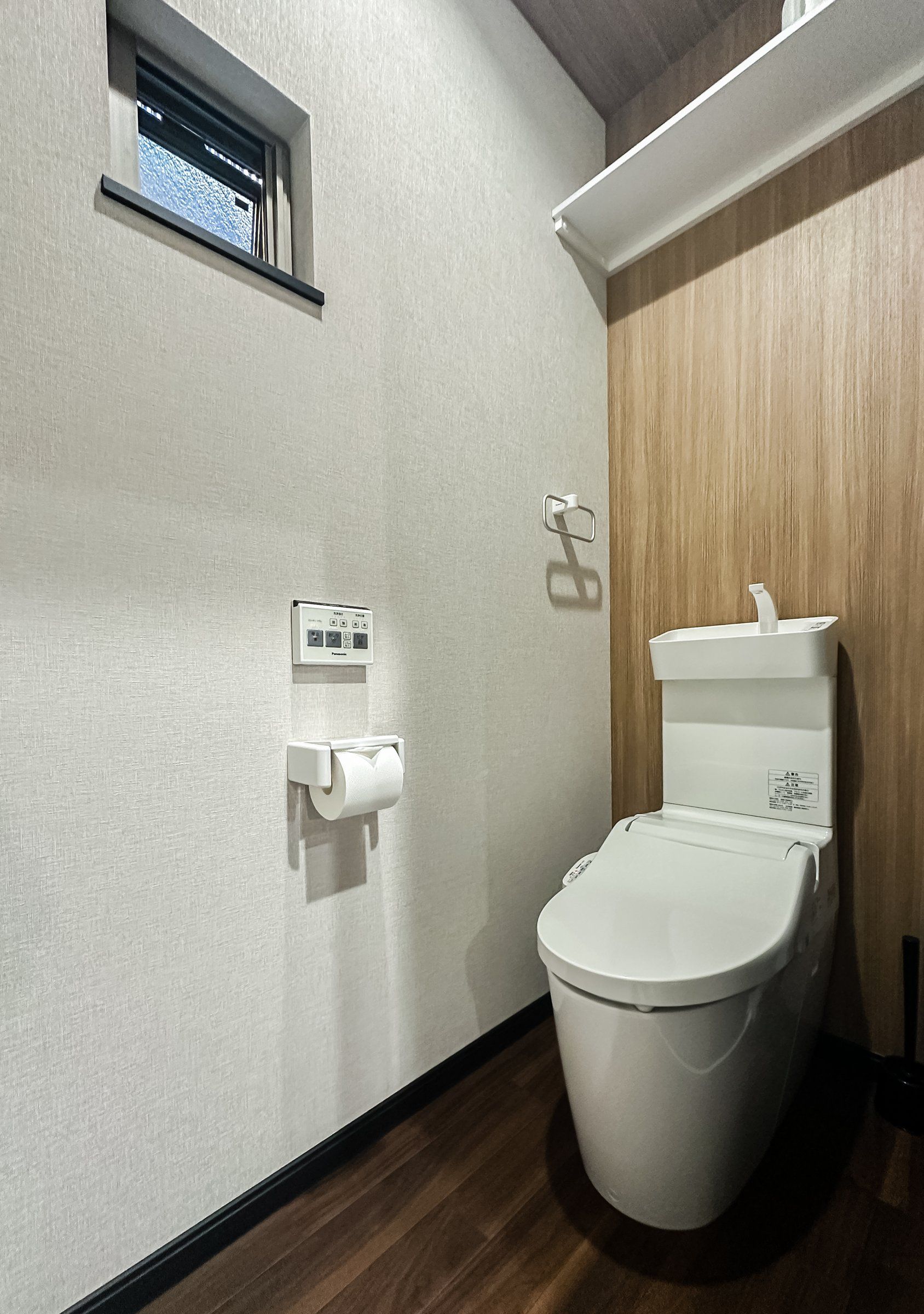 A modern bathroom with a toilet, a paper towel dispenser, and a power outlet on the wall.