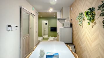 Habitación de hotel con una mesa de comedor, sillas, un minibar, un televisor y una planta en la pared.