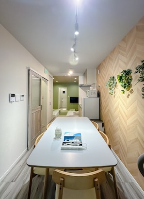 A hotel room with a dining table, chairs, a minibar, a television, and a plant on the wall. - HANASTAY KAERU (Osaka)