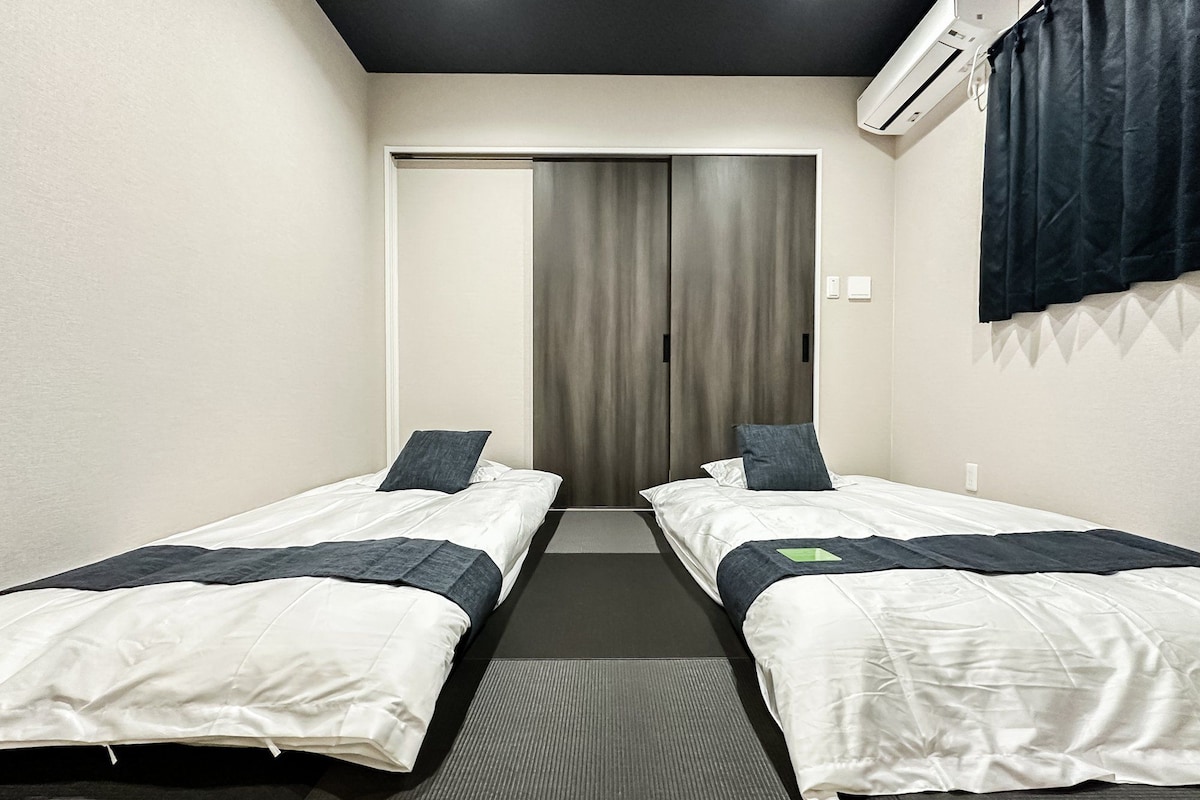 A hotel room with two single beds, a dark ceiling, a door with a curtain, and an air conditioning unit.