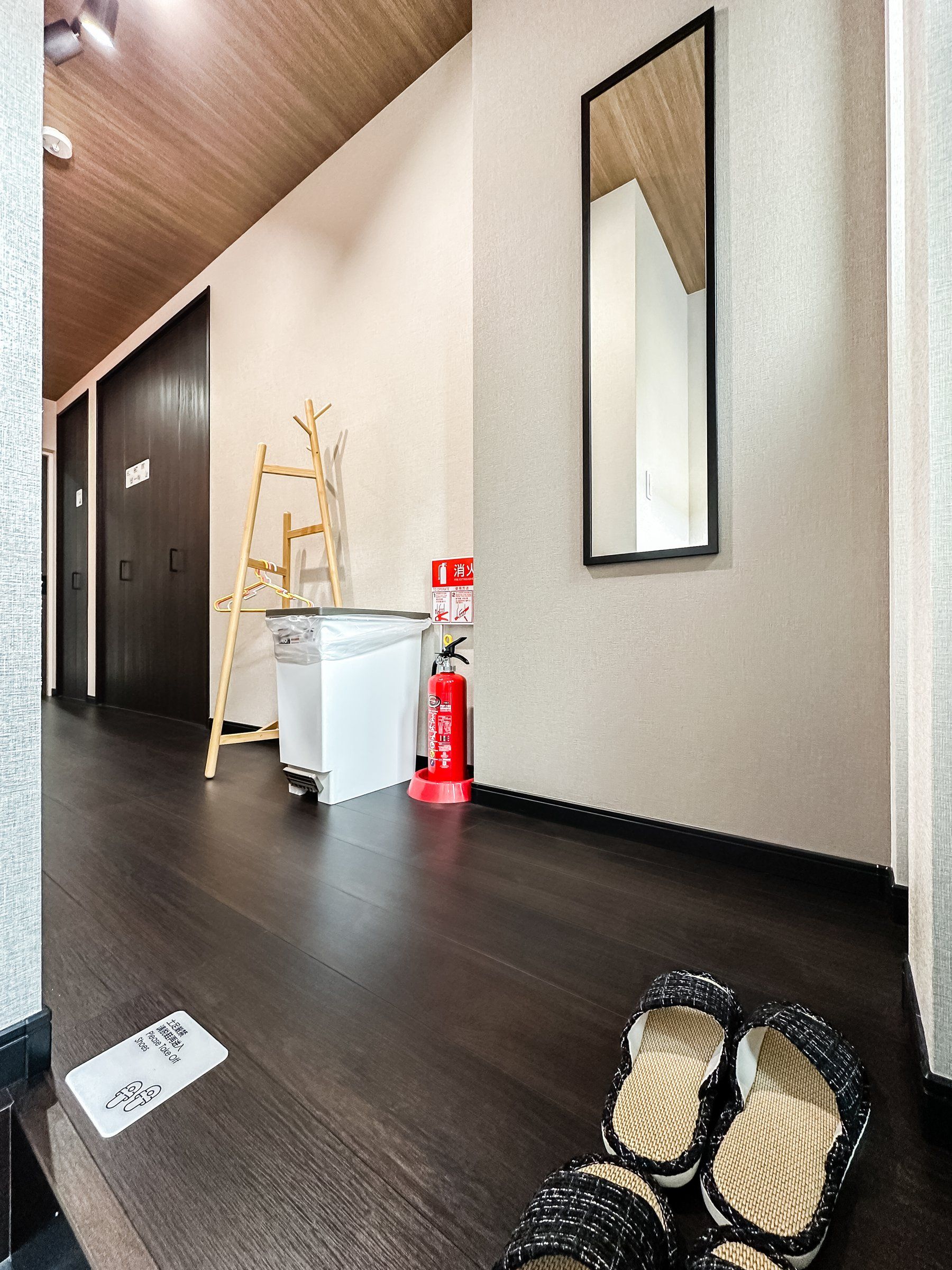 A hotel corridor with a wooden floor, a fire extinguisher, a ladder, and a mirror on the wall.