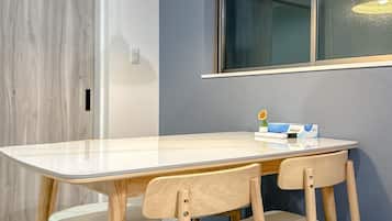 Un comedor con una mesa rectangular, cuatro sillas de madera, una lámpara colgante y un ventanal con vistas.