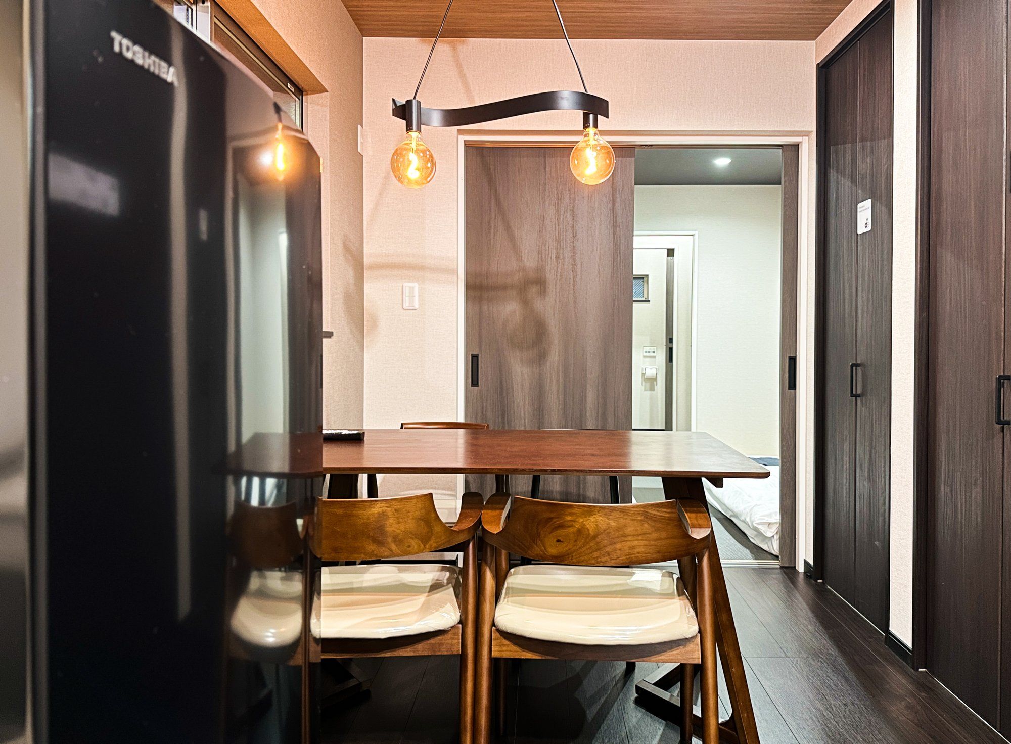 A modern kitchen with a wooden table, two chairs, and pendant lighting.