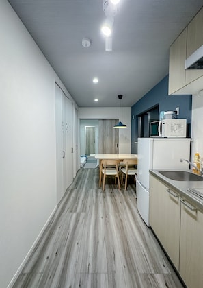 A modern kitchen with a dining area, wooden flooring, and a view into a bedroom. - HANASTAY KAERU (Osaka)