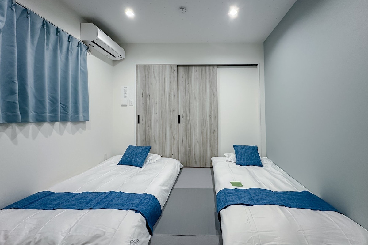 A room with two beds, a wooden wardrobe, and an air conditioning unit.