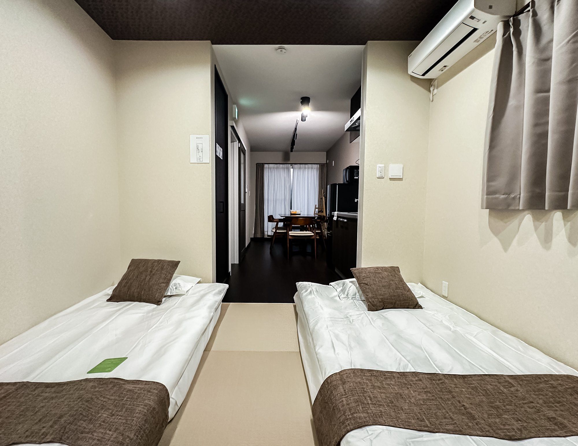 A hotel room with two single beds, a small kitchenette, a dining area, and a bathroom.