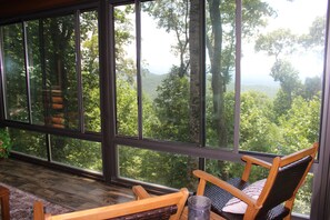 A room with large windows, a wooden chair, and a rug. - 3-bedroom cabin in beautiful Ellijay with cool mountain vibes (Ellijay)