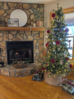 A cozy living room with a stone fireplace, a decorated Christmas tree, and plaid-patterned cushions. - 3-bedroom cabin in beautiful Ellijay with cool mountain vibes (Ellijay)