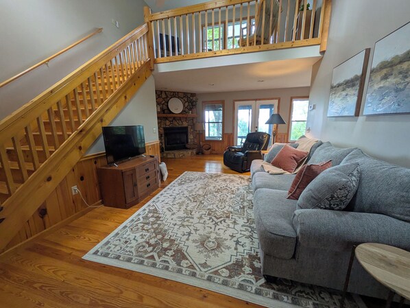 A spacious living room with a wooden staircase, a fireplace, a leather recliner, and a grey sofa with patterned cushions. - 3-bedroom cabin in beautiful Ellijay with cool mountain vibes (Ellijay)