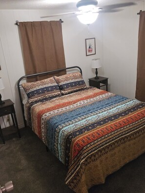 A single-bed room with a patterned bedspread, a bedside table with a lamp, and a ceiling fan. - The Colorado Cowboy Hideaway - a 3 bed, 2 bath gem located in Bullhead City! (Bullhead City)