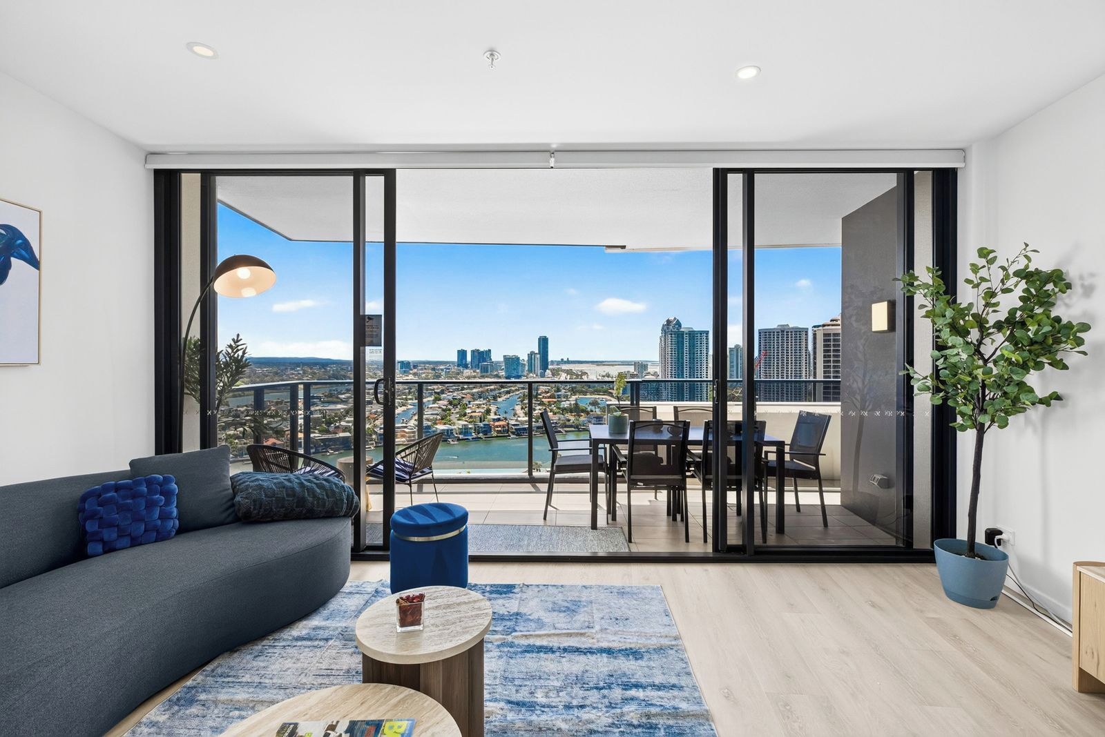 Una sala de estar moderna con un sofá, una mesa de centro y vistas a un paisaje urbano a través de puertas correderas amplias.