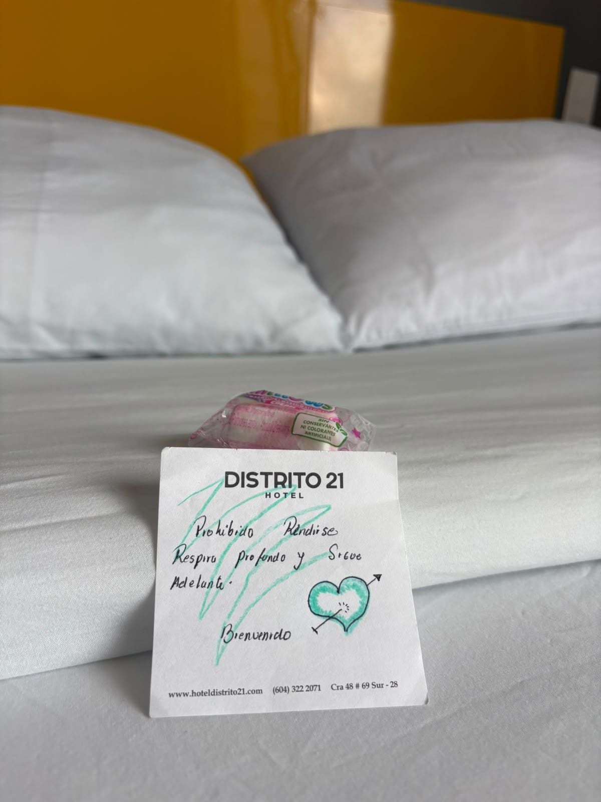 A hotel room with a bed, pillows, and a welcome card on the bed.