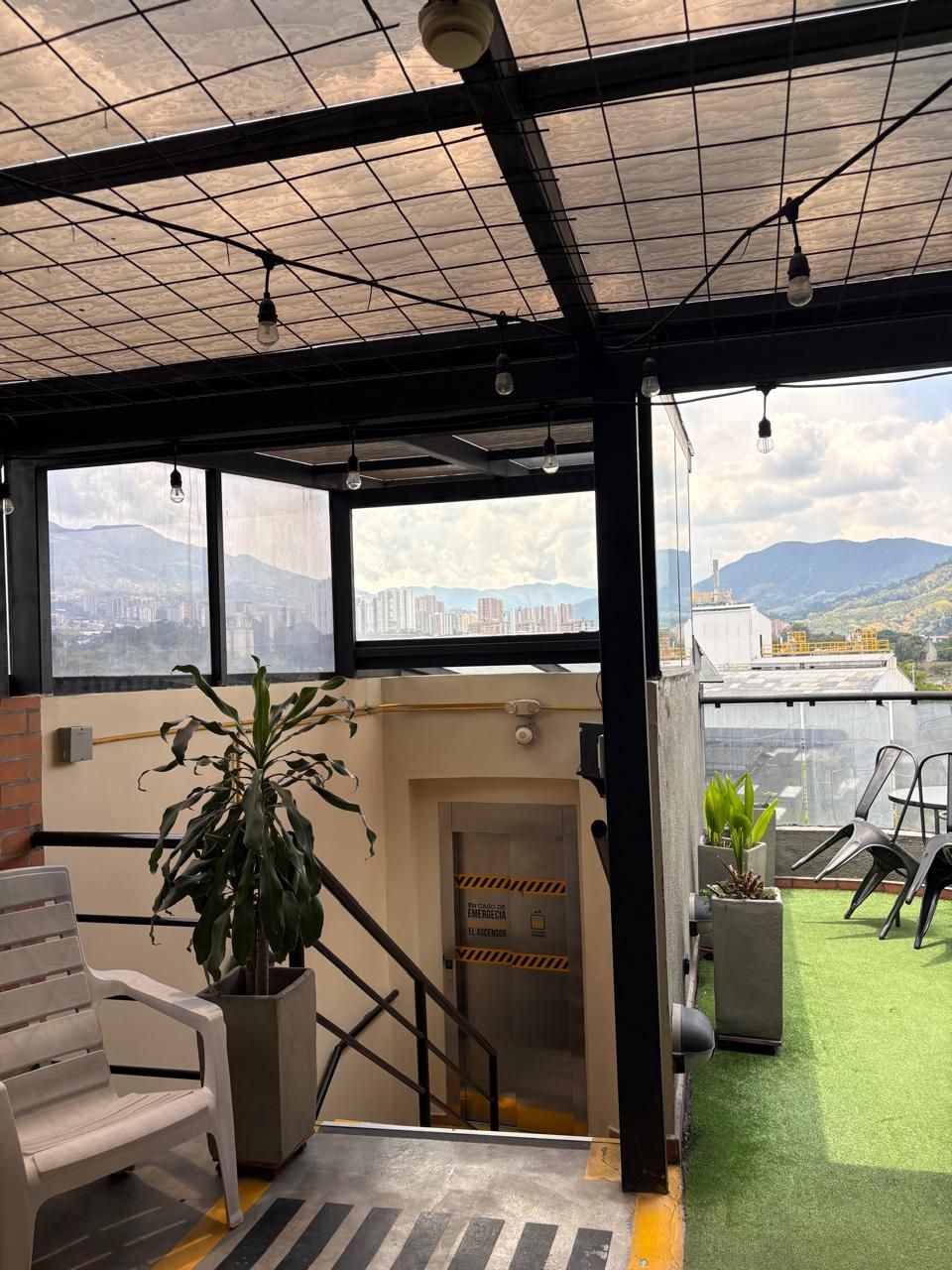 Un hall d’hôtel avec un escalier menant à l’étage supérieur, une plante en pot, un banc et une vue sur le paysage urbain à travers de grandes fenêtres.