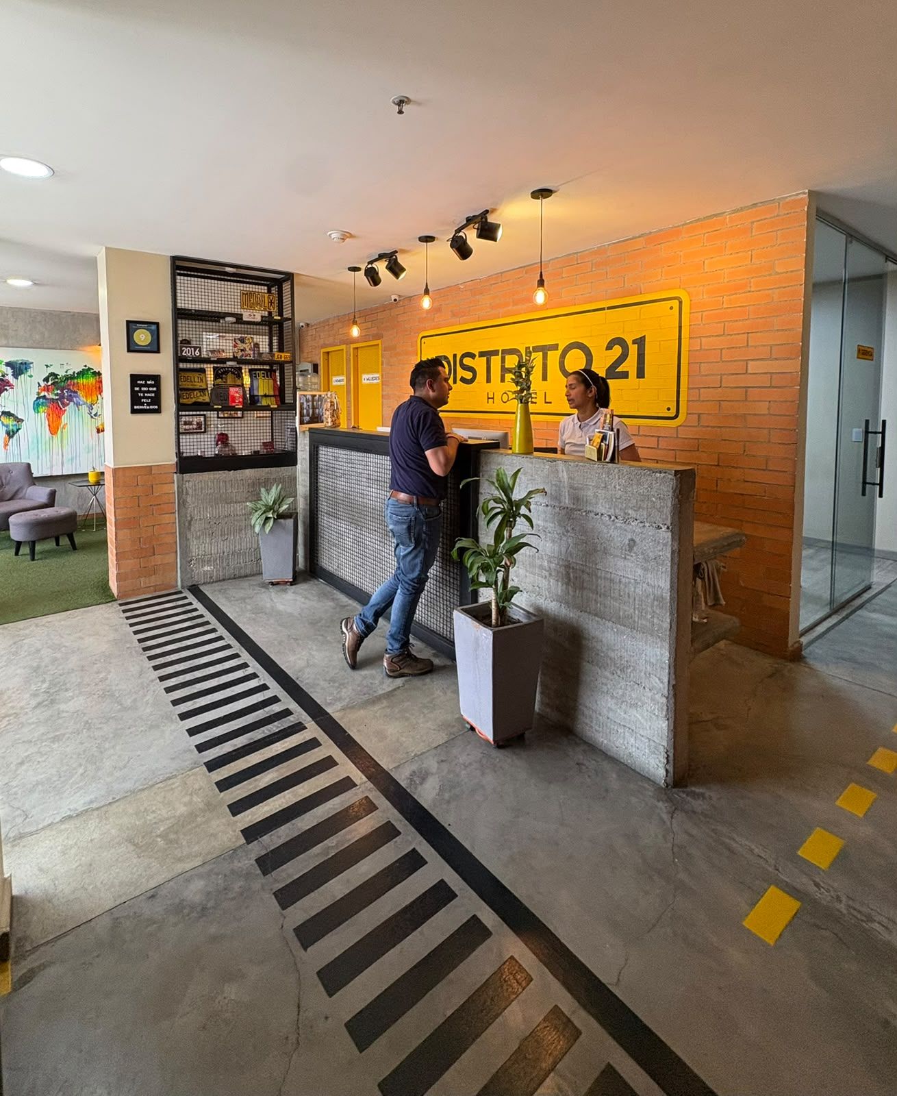 A reception desk with a sign reading 'DISTRITO 21 HOTEL' and a man approaching it.
