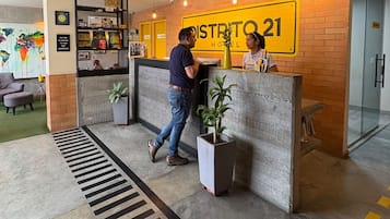 A reception desk with a sign reading 'DISTRITO 21 HOTEL' and a man approaching it.