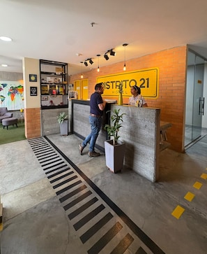 Un mostrador de recepción con un cartel que dice 'DISTRITO 21 HOTEL' y un hombre acercándose.