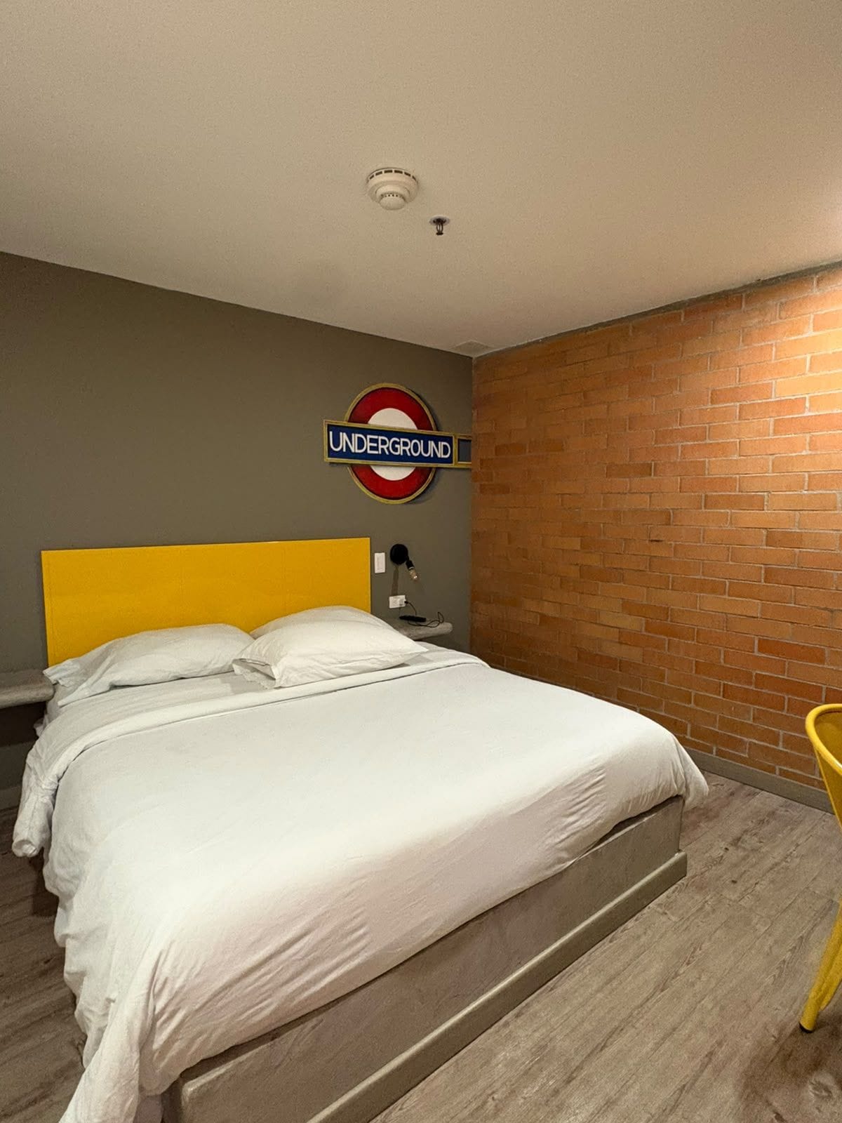 A bedroom with a bed, a brick wall, and a sign indicating an underground station.