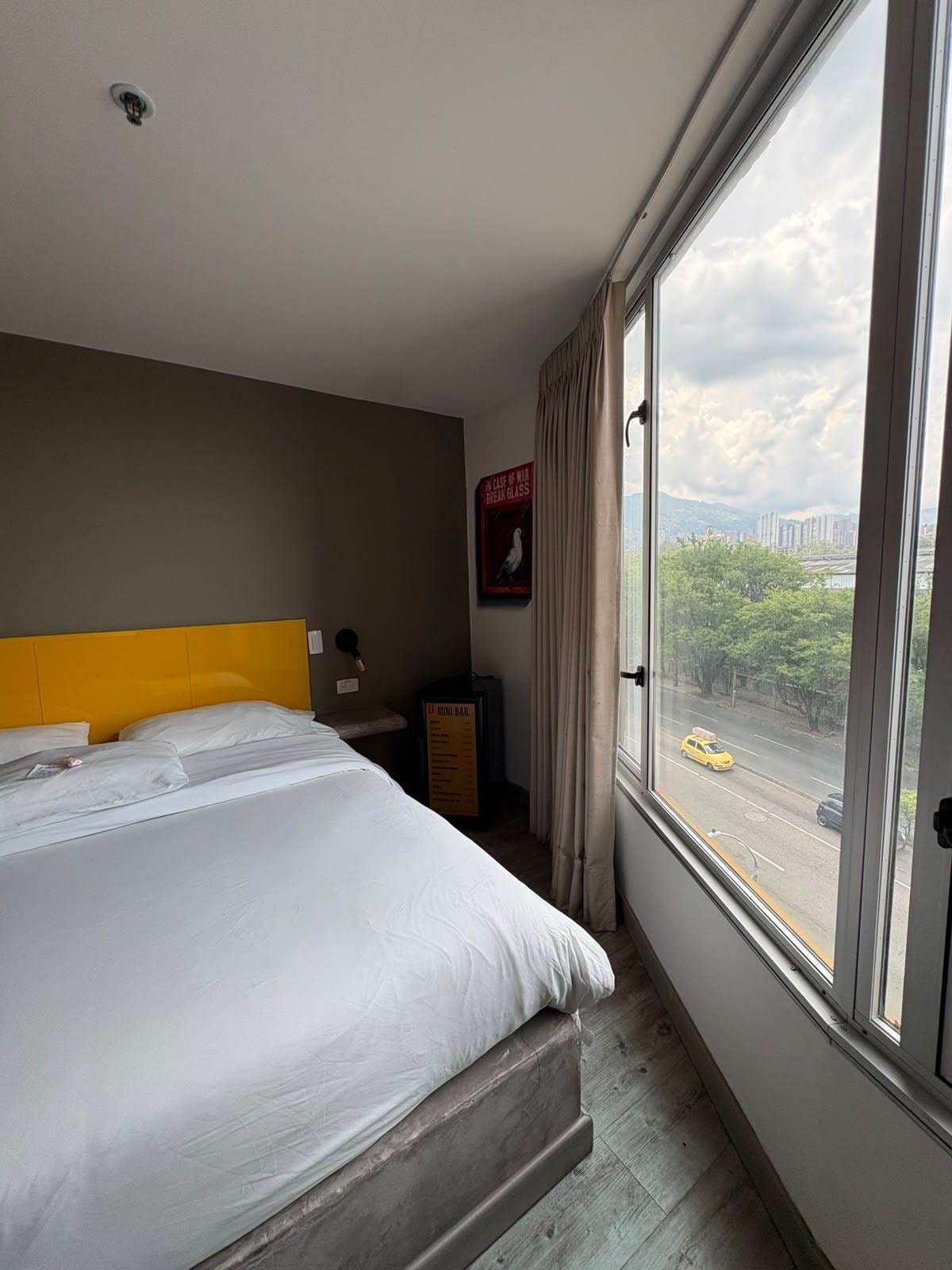 Una habitación de hotel con una cama grande, vistas a una calle de la ciudad y un mini bar.