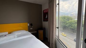 Una habitación de hotel con una cama grande, vistas a una calle de la ciudad y un mini bar.