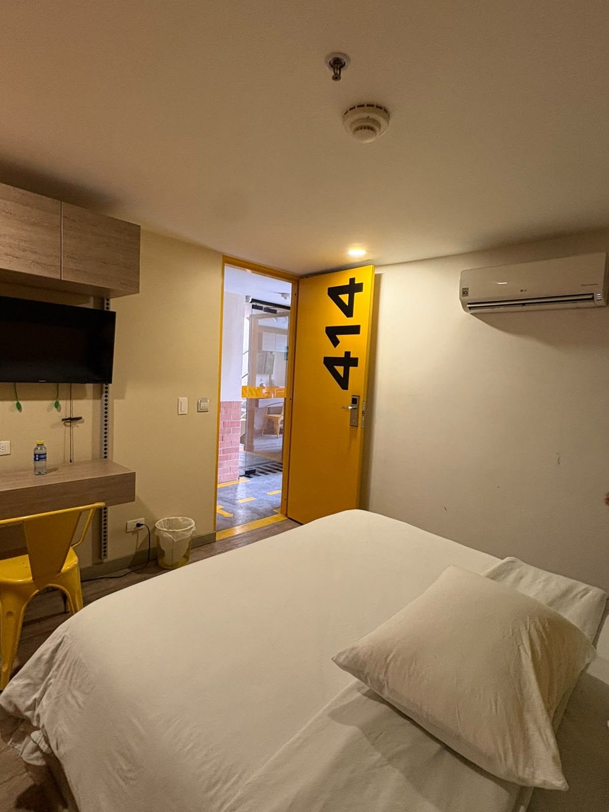Una camera d'albergo con un letto, una scrivania, una sedia, un condizionatore d'aria e una porta contrassegnata dal numero 414.