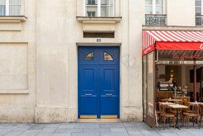Eine blaue Doppeltür mit einem kleinen Fenster, darüber die Zahl '168' und eine rot-weiß gestreifte Markise zur Rechten.