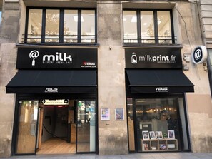 Ein Gebäude mit zwei Schaufenstern, eines beschriftet mit 'milk' und das andere mit 'milkprint.fr', wobei beide eine 24-Stunden-Betreuung anbieten.