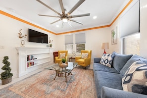 A living room with a ceiling fan, a fireplace, a sofa, a coffee table, and a bookshelf. - Charming Updated Historic Home, Walk to Downtown, Shops, and Restaurants, $300 in Free Tickets! (St. Augustine)