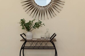 A wall-mounted mirror with a sunburst design, a potted plant, a glass decanter, and a small table with a book and glass. - Walk to Downtown, Shops, Restaurants! Charming Historic Home, Screened Porch, $300 in Free Tickets! (St. Augustine)