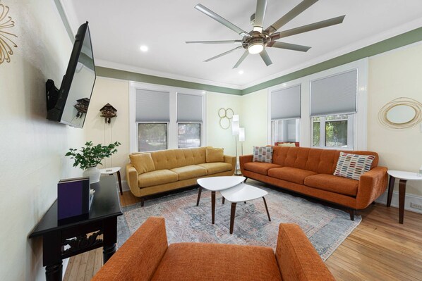 A living room with two sofas, a coffee table, a TV, a ceiling fan, and a decorative wall piece. - Walk to Downtown, Shops, Restaurants! Charming Historic Home, Screened Porch, $300 in Free Tickets! (St. Augustine)