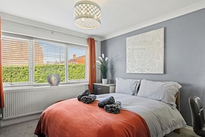 Une chambre à coucher avec un lit, une table de chevet, une plante en pot et une fenêtre avec des stores.