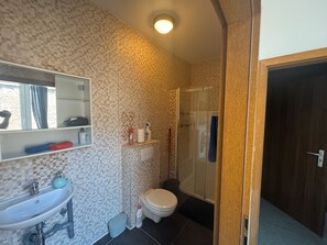 A bathroom with a tiled wall, a sink, a toilet, and a shower area. - Bright 1-bedroom apartment in Outremeuse, self check-in, near city centre (Liège)
