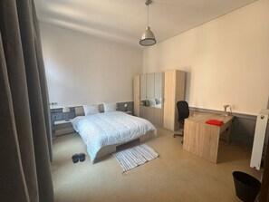 A bedroom with a bed, a desk, a chair, a wardrobe, and a hanging light fixture. - Bright 1-bedroom apartment in Outremeuse, self check-in, near city centre (Liège)