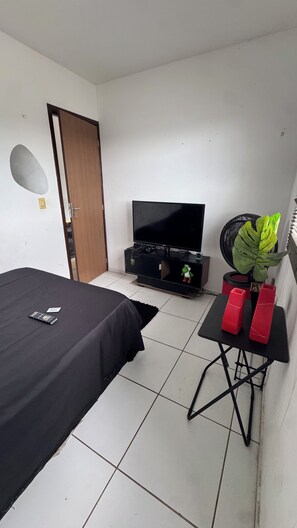A small room with a bed, a television, a desk with a plant, and a door. - Room with pool view in gated community (Vitória de Santo Antão)