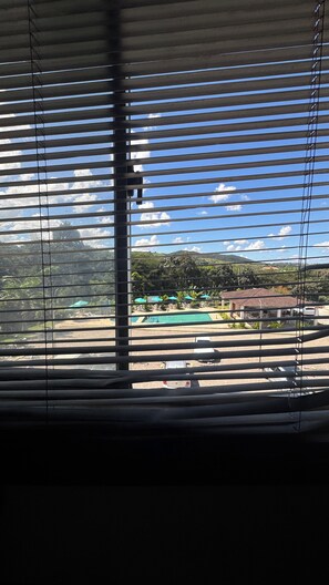 A view through window blinds of a pool area with a mountain backdrop. - Room with pool view in gated community (Vitória de Santo Antão)