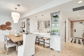 Eine moderne Küche mit einer zentralen Kochinsel, Pendelleuchten und einem Essbereich mit einem Holztisch und gepolsterten Stühlen.