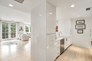 Eine moderne Küche mit weißen Schränken, einer Edelstahlspüle und einem Essbereich mit einem weißen Sofa sowie einer Glastür, die auf eine Terrasse führt.