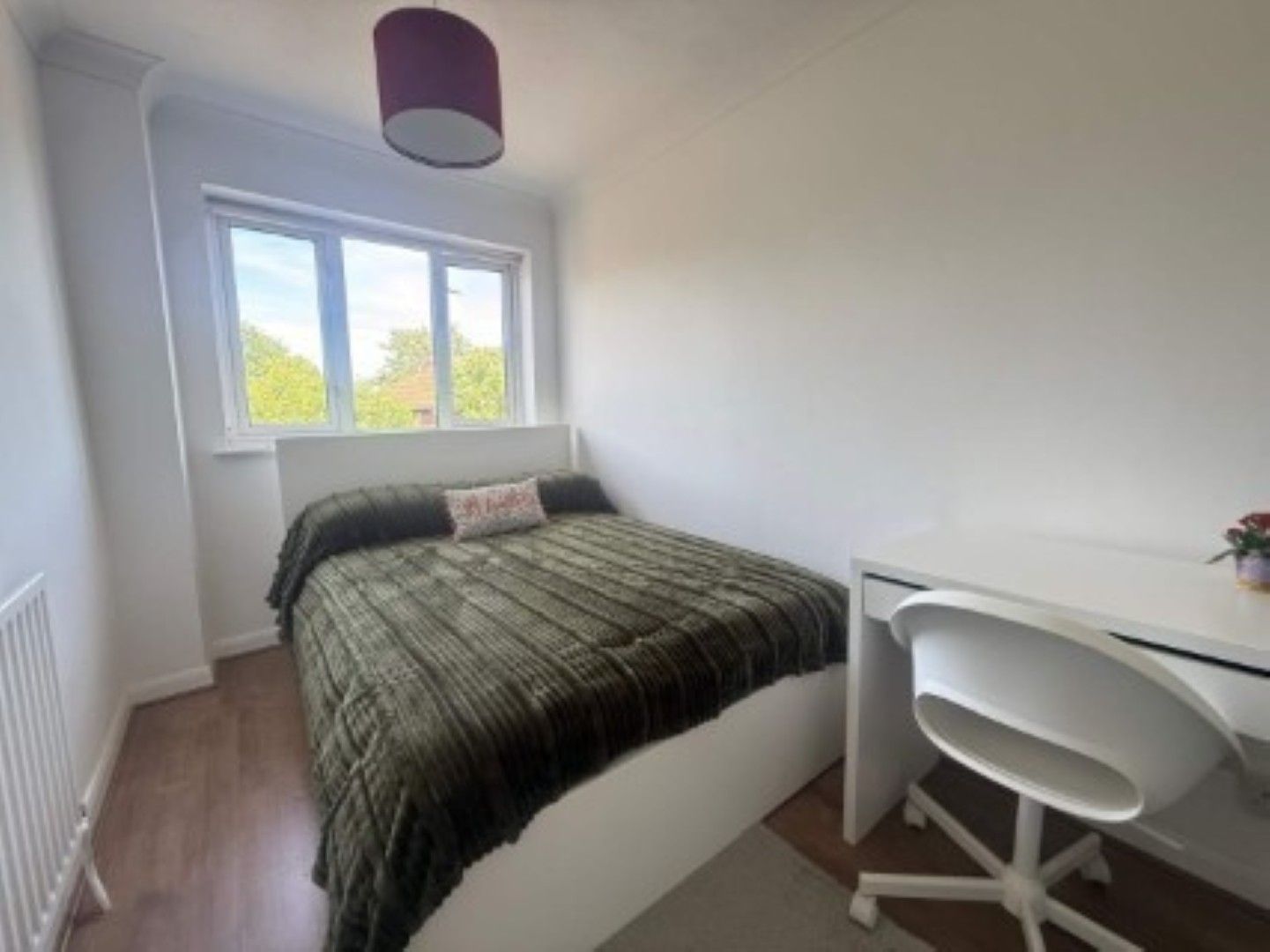 A bedroom with a bed, a desk, and a window.
