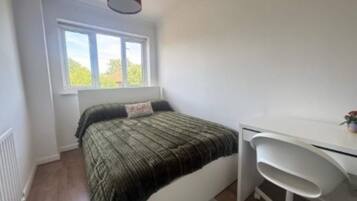 A bedroom with a bed, a desk, and a window.