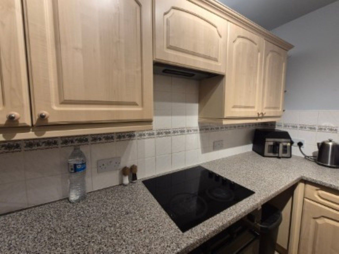 A kitchen with granite countertops, a black induction cooktop, wooden cabinets, and a coffee maker.